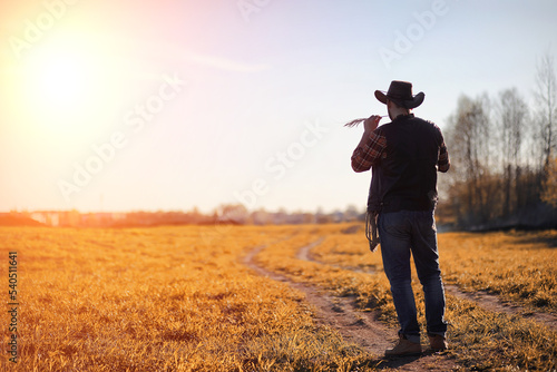A man cowboy hat and a loso in the field. American farmer in a field wearing a jeans hat and with a loso. A man is walking across the field in a hat © alexkich