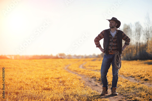 A man cowboy hat and a loso in the field. American farmer in a field wearing a jeans hat and with a loso. A man is walking across the field in a hat