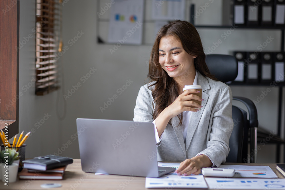 Beautiful young smiling asian multiethnic woman working on laptop and drinking coffee in at workplace, Asia woman working document finance and calculator in her home office. Enjoying time at home.
