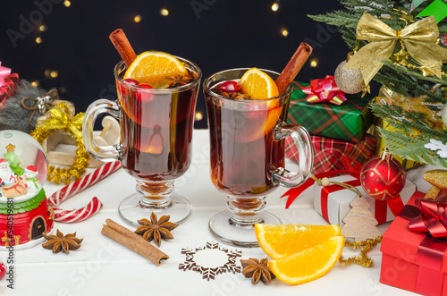 Traditional hot Christmas mulled wine with spices and fruits in mugs on a white wooden table near the Christmas tree