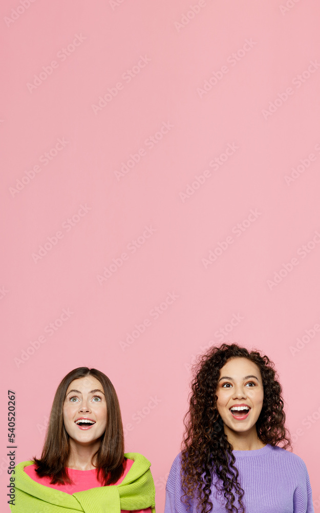 Young two friends surprised amazed shocked women 20s wears green purple shirts looking overhead on workspace area mock up together isolated on pastel plain light pink color background studio portrait. Young two friends surprised amazed shocked women 20s wears green purple shirts looking overhead on workspace area mock up together isolated on pastel plain light pink color background studio portrait.