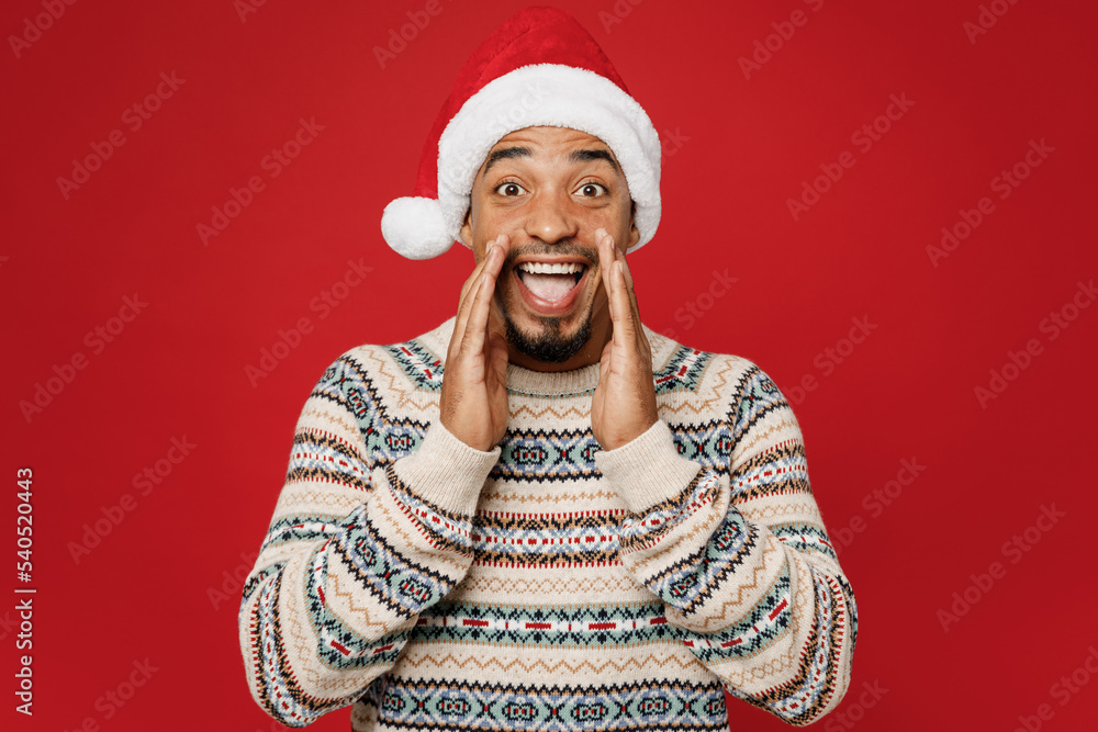 Merry promoter young man in Christmas sweater Santa hat posing scream sharing hot news about sales discount with hands near mouth isolated on plain red background Happy New Year 2023 holiday concept Merry promoter young man in Christmas sweater Santa hat posing scream sharing hot news about sales discount with hands near mouth isolated on plain red background Happy New Year 2023 holiday concept