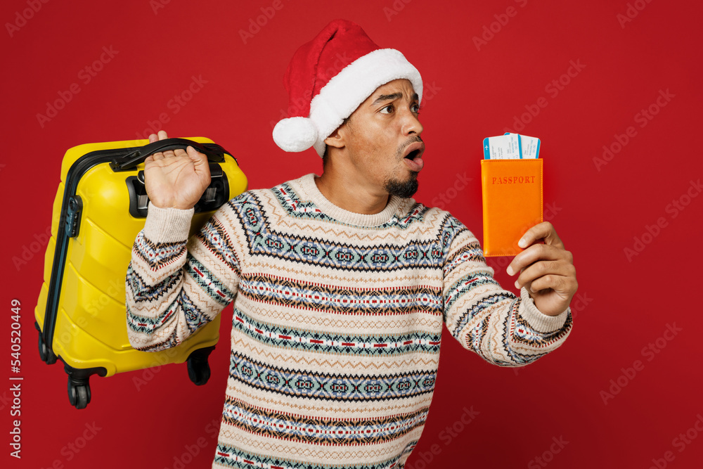 Traveler man in sweater Santa hat hold valise run passport ticket isolated on plain red background Tourist travel abroad in free spare time rest getaway Air flight trip journey New Year 2023 concept Traveler man in sweater Santa hat hold valise run passport ticket isolated on plain red background Tourist travel abroad in free spare time rest getaway Air flight trip journey New Year 2023 concept