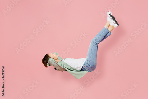 Full body side view young happy woman 20s she wear green shirt white t-shirt fly up hover over air fall down isolated on plain pastel light pink background studio portrait. People lifestyle concept.