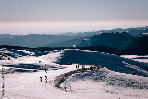 Panoramic view over the ski slope Poiana Brasov ski resort in Transylvania, Pine forest covered in snow on winter season,Mountain landscape in winter with the Bucegi Mountains in the background. photo