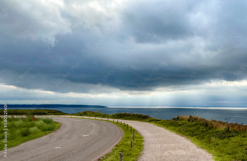 The road with a view of the cloudy sky and the sea. Plévenon, Cap Frehel, Bretagne, France. 