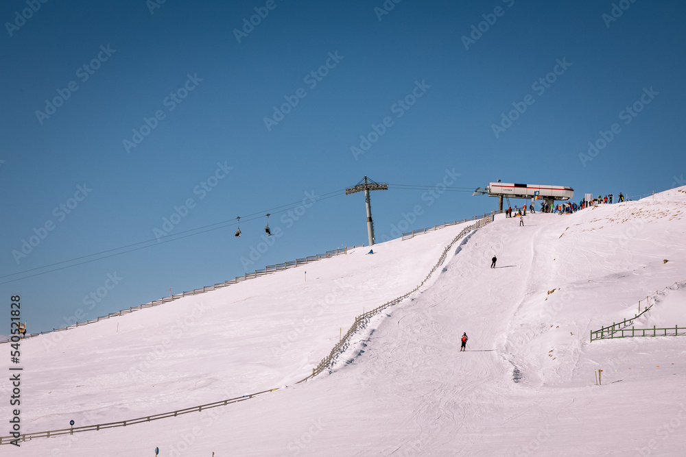 Obraz premium Panoramic view over the ski slope Poiana Brasov ski resort in Transylvania, Pine forest covered in snow on winter season,Mountain landscape in winter with the Bucegi Mountains in the background.