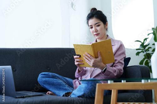 Portrait of a self-employed Asian woman holding a notebook and using a computer doing video conference at home