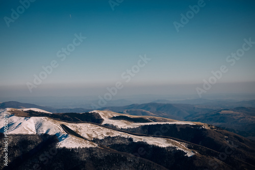 Panoramic view over the ski slope Poiana Brasov ski resort in Transylvania, Pine forest covered in snow on winter season,Mountain landscape in winter with the Bucegi Mountains in the background. photo