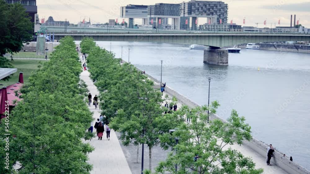Diverse people walk on Rhine boulevard promenade at sunset with view of ...