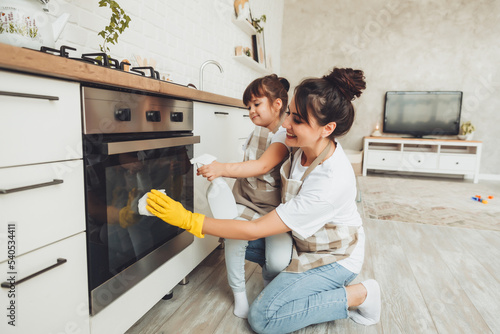 A little girl and her mother are cleaning the kitchen. a woman and a child wipe the oven in the kitchen. house cleaning. helping mom.