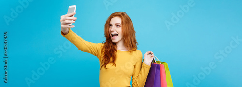 Shopping Concept - Close up Portrait young beautiful attractive redhair girl smiling looking at camera with white shopping bag and selfie. Blue Pastel Background. Copy space