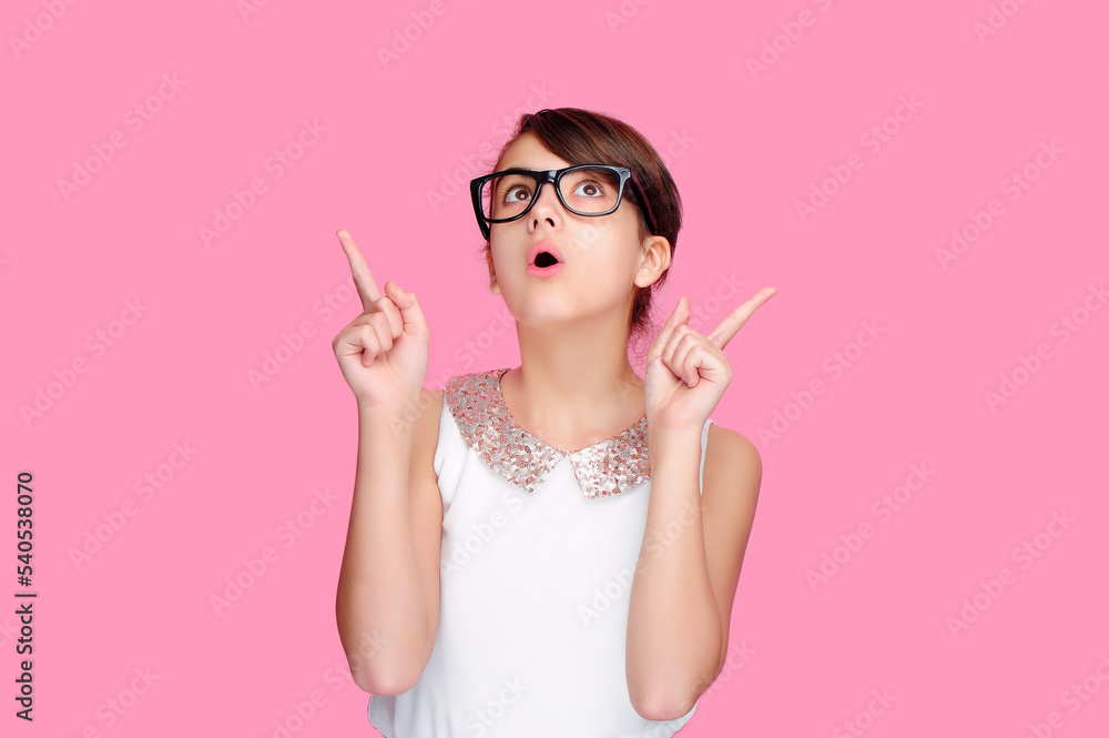 Amazed teen girl wearing glasses pointing up to the copy space area Amazed teen girl wearing glasses pointing up to the copy space area