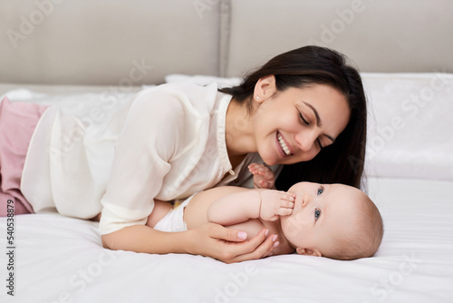 mother plays with her baby girl in the bedroom.