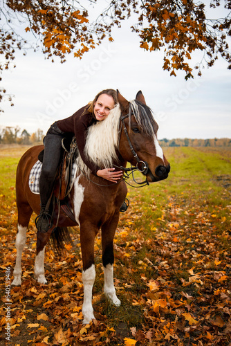 beautiful slim smiling brunette woman riding horse in autumn field