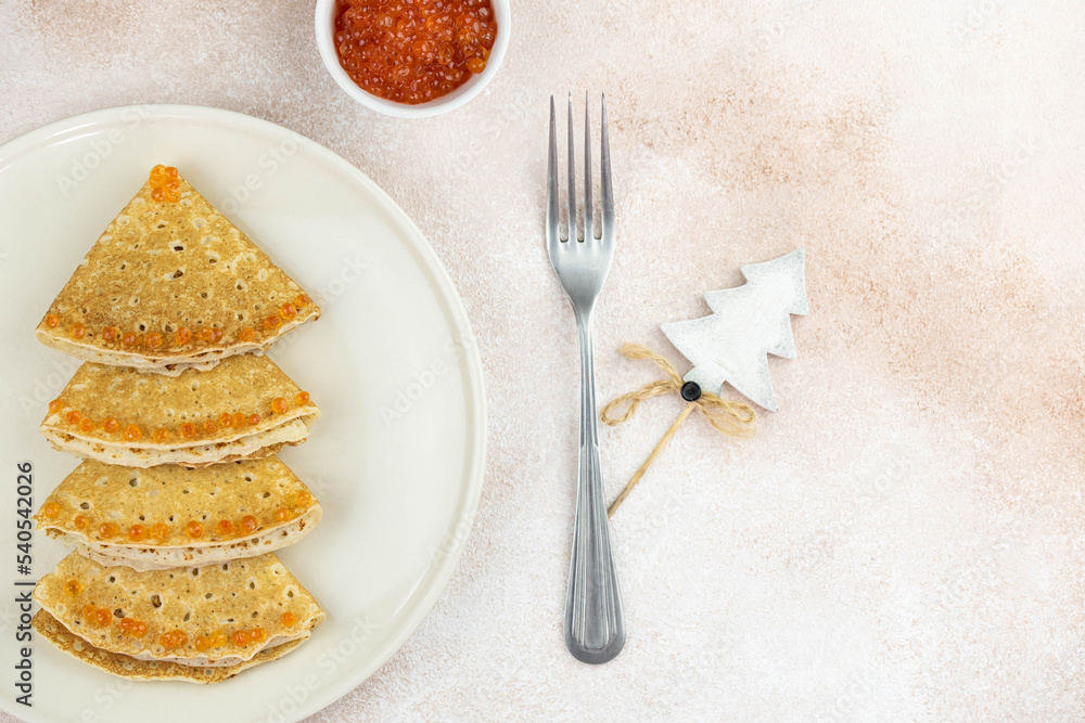 Christmas and New year tree shaped pancakes or crepes with red caviar decorations on light colored background. Holiday homemade food. Flat lay top view. Christmas food for children and kids. Christmas and New year tree shaped pancakes or crepes with red caviar decorations on light colored background. Holiday homemade food. Flat lay top view. Christmas food for children and kids.