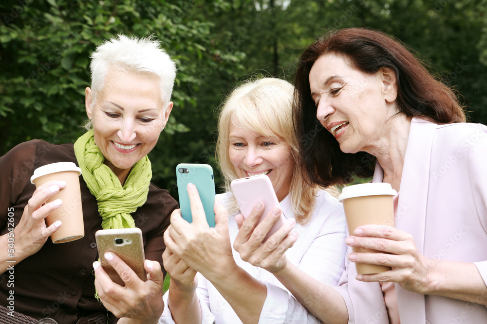 Charming old women laugh merrily and look at the screens of their smartphones. Charming old women laugh merrily and look at the screens of their smartphones.