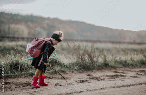 Mała dziewczynka z plecakiem rysuje patykiem po ziemi