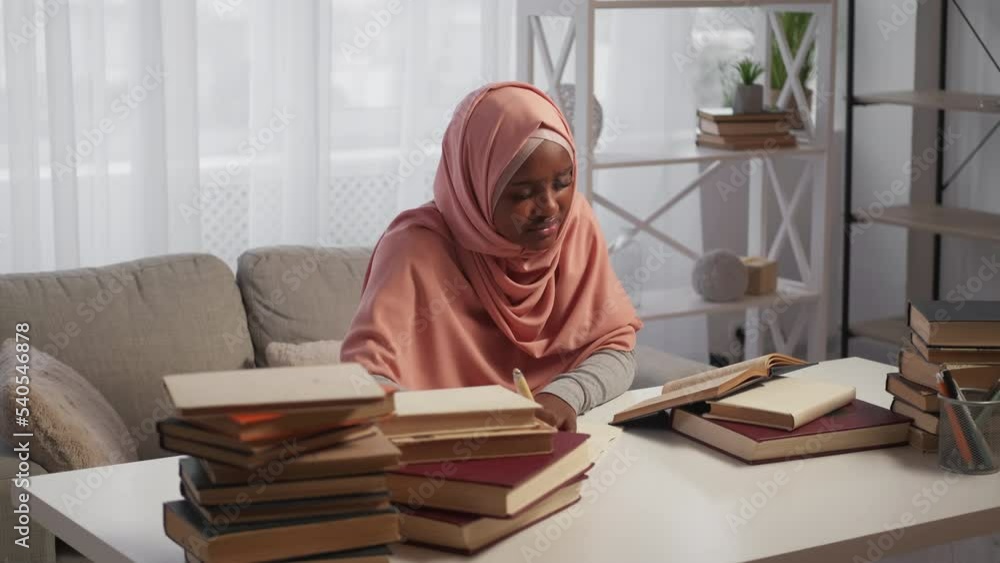 Exhausted education. Sleepy woman. Exam preparation. Tired lady in hijab making notes studying with pile books in light room interior. Exhausted education. Sleepy woman. Exam preparation. Tired lady in hijab making notes studying with pile books in light room interior.