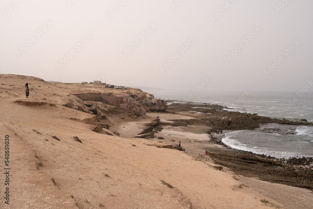 Woman solo traveler alone in empty beach with mountains, rocks and waves looking at sea in agadir desert, morocco Woman solo traveler alone in empty beach with mountains, rocks and waves looking at sea in agadir desert, morocco