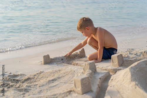 Little boy plays on the beach in Dubai and builds a sand castle