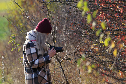 Kobieta fotograf, blond włosy wykonująca zdjęcia przyrody jesienią.