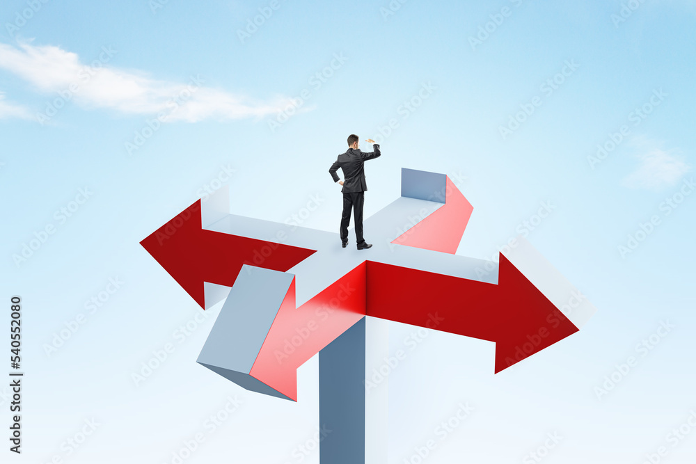 Young businessman standing on abstract arrow sign and looking into bright blue sky. Different direction, choice and success concept. Young businessman standing on abstract arrow sign and looking into bright blue sky. Different direction, choice and success concept.