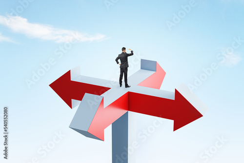 Young businessman standing on abstract arrow sign and looking into bright blue sky. Different direction, choice and success concept.
