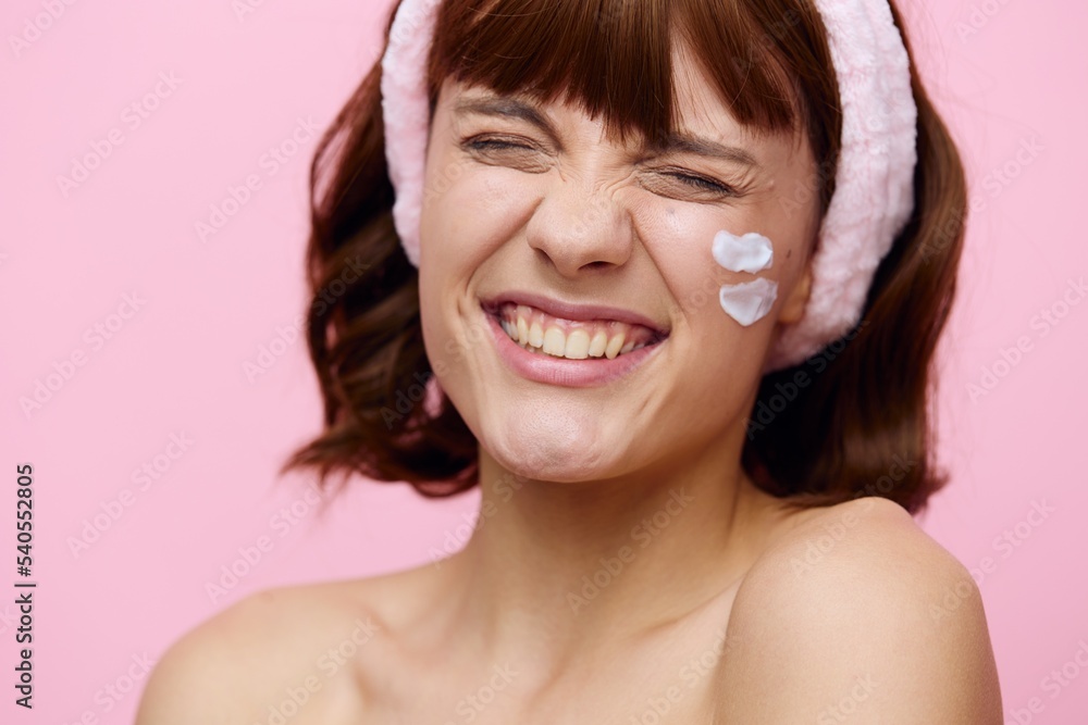 a close portrait on a pink background, of a funny, attractive woman with cream on her face, smiling broadly, closing her eyes with delight a close portrait on a pink background, of a funny, attractive woman with cream on her face, smiling broadly, closing her eyes with delight