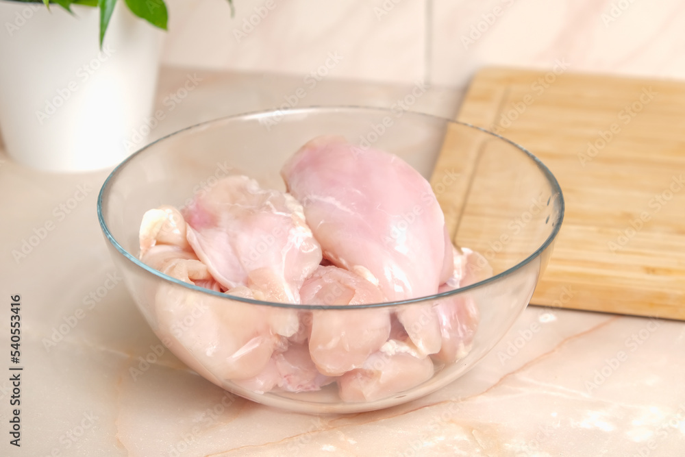Defrosted raw chicken fillet in a glass bowl. Fresh raw chicken breast for cooking chopped chicken cutlets. Glass bowl and wooden cutting board for slicing chicken fillet.