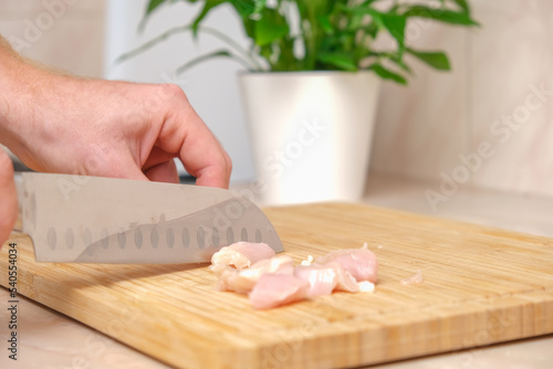 Defrosted raw chicken fillet on cutting board. Slicing fresh raw chicken breast with sharp knife for cooking chopped chicken cutlets on a bamboo wooden cutting board for slicing. Kitchen knife test.
