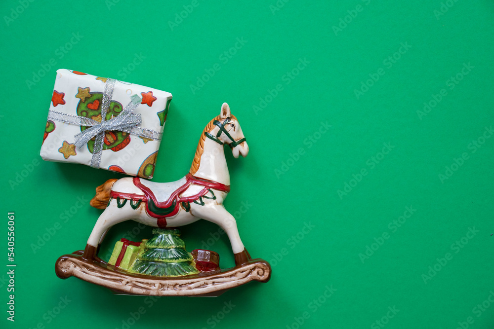 toy horse porcelain figure with wrapped gift box, merry christmas and happy new year decorations on a green background, festive holiday surprise, copy space, gifts delivery service