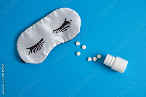 sleep mask with painted eyelashes and pills for insomnia on a blue background
