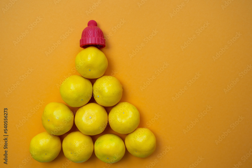 tangerine pyramid with red hat on top, imitation of Christmas tree, fresh yellow and orange citrus fruits, on colored background, copy space, happy holidays, source of vitamin c in shop tangerine pyramid with red hat on top, imitation of Christmas tree, fresh yellow and orange citrus fruits, on colored background, copy space, happy holidays, source of vitamin c in shop