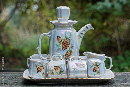 a coffee set from old porcelain dishes with a colored teapot and cups on a tray stand on a table on the street on a green background © butus
