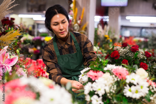 Asian woman florist in apron taking care of flowers in salesroom of floral shop. © JackF