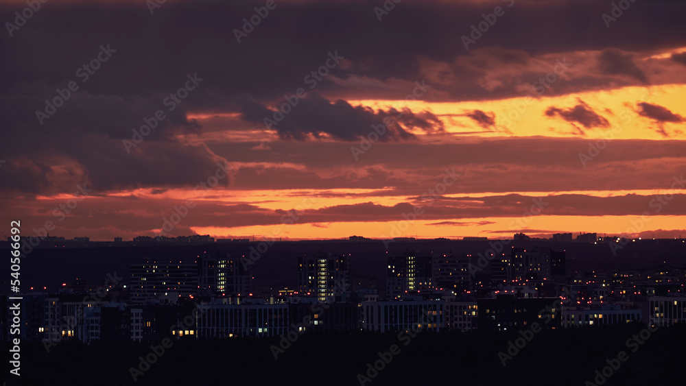 Illuminated windows of city buildings at dusk, night cityscape. Cloudy sky and evening city