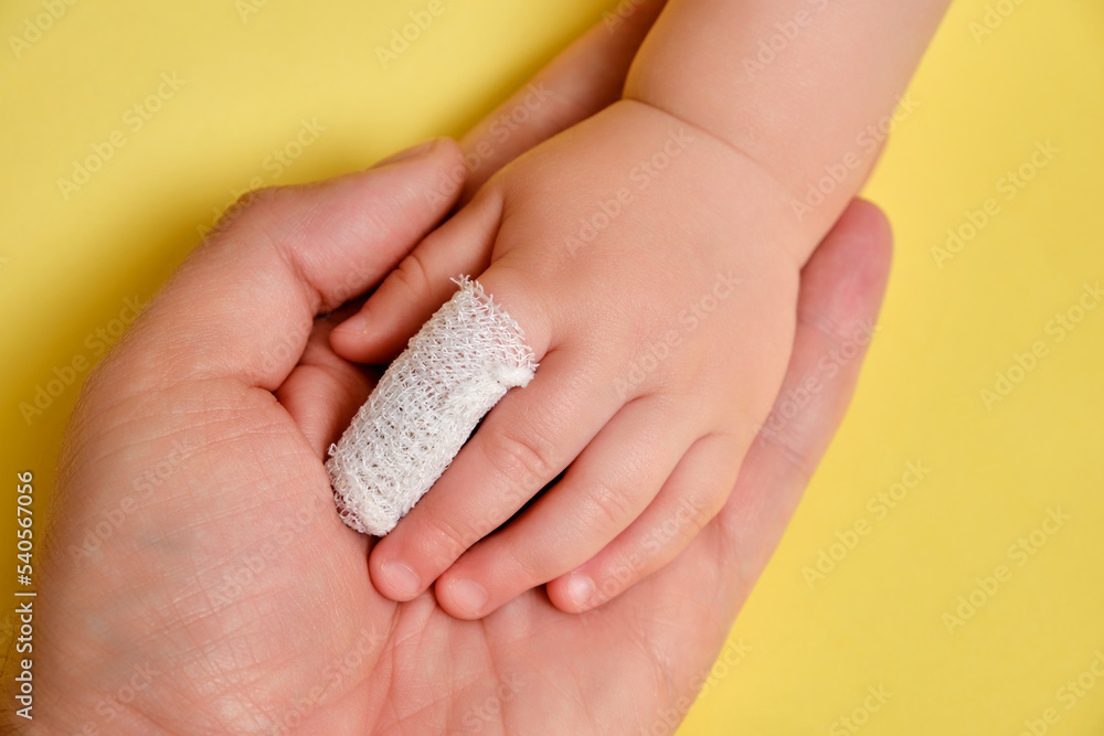 Large hand of father man and small hand of baby with bandaged finger,  yellow studio background.