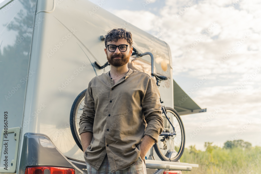 Medium outdoor portrait of bearded millennial hipster man in front of his unconventional four-wheel house. Compering and biking. Positive emotions. . High quality photo
