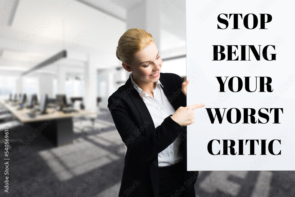 smiling businesswoman in front of a wall with the message STOP BEING YOUR WORST CRITIC smiling businesswoman in front of a wall with the message STOP BEING YOUR WORST CRITIC