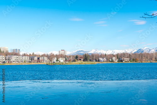 Westchester Lagoon with small island on the lake and row of duplex houses with downtown Anchorage buildings office towers in background © trongnguyen