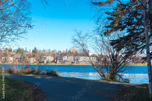 View lakeside coastal trail to row of duplex houses with downtown Anchorage buildings in background from Westchester Lagoon park © trongnguyen