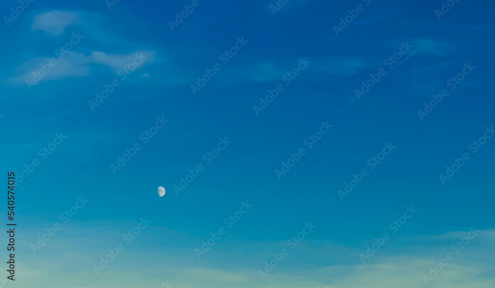 Luna bianca nel cielo azzurro e scia di aereo