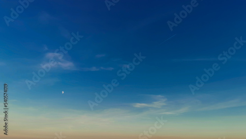 Luna bianca nel cielo azzurro e scia di aereo