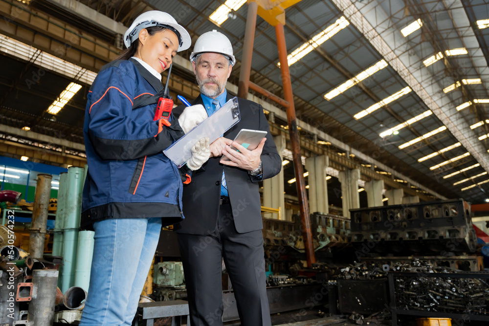 A business man inspects the work of an on-site worker at an old factory for rehearsing train engines.