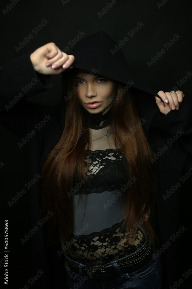 portrait of a beautiful young red-haired girl on a dark black background in the studio, with a cleavage and big breasts in black hood, hoodie portrait of a beautiful young red-haired girl on a dark black background in the studio, with a cleavage and big breasts in black hood, hoodie