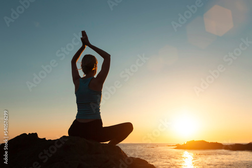 Yoga woman, meditating on the ocean beach during a beautiful sunset.