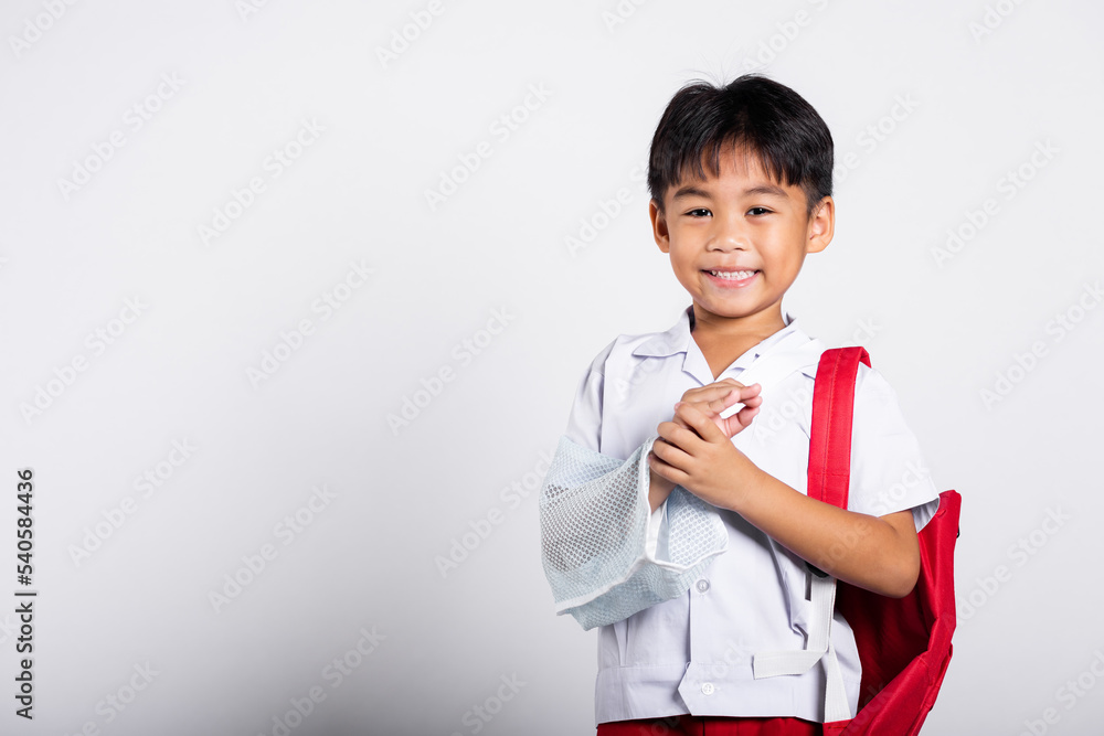 Asian student kid boy wearing student thai uniform accident broken bone wearing splint arm plaster fiberglass cast covering arm in cast at studio shot isolated on white background, back to school Asian student kid boy wearing student thai uniform accident broken bone wearing splint arm plaster fiberglass cast covering arm in cast at studio shot isolated on white background, back to school