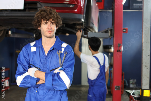 Caucasian technician engineer or worker man uniform standing and holding wrench checking maintenance a car service with confident at repair garage station. Concept of car center repair service.