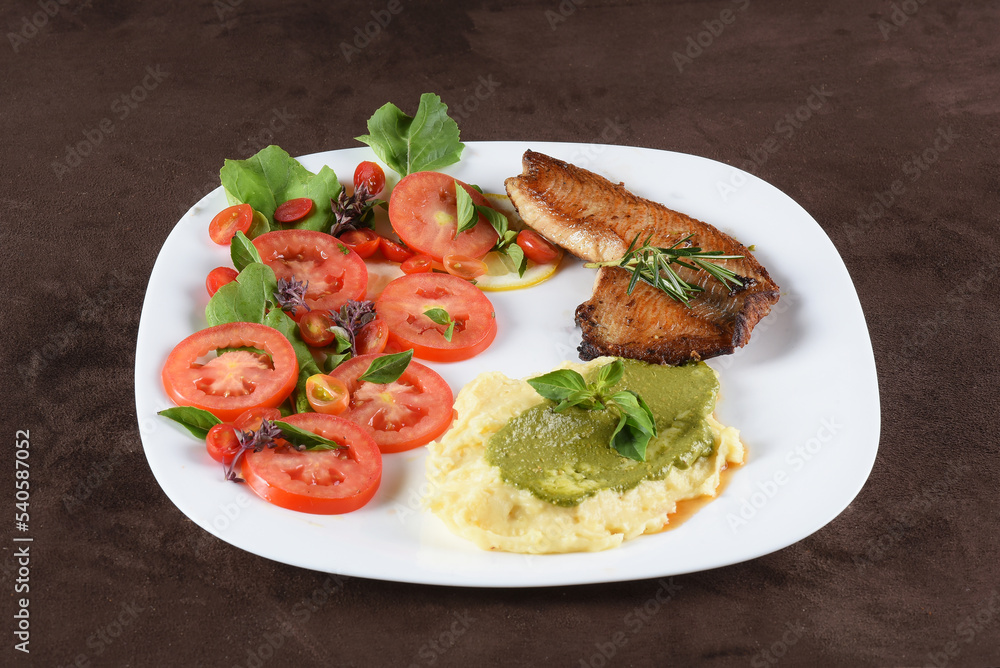 fried tilapia fish filet served on plate with tomato salad and mashed potatoes with herb pesto fried tilapia fish filet served on plate with tomato salad and mashed potatoes with herb pesto